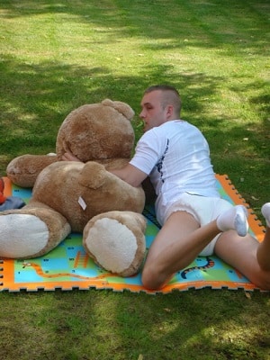 Young man lying asleep in Grass with a teddy bear